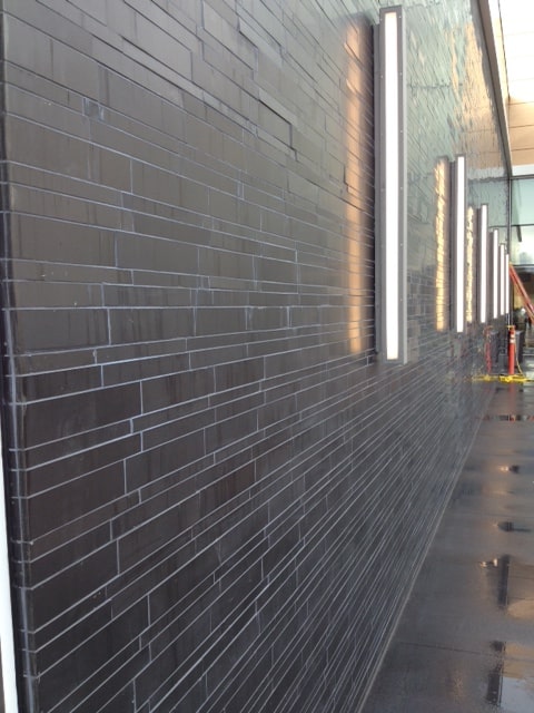 Norstone Lynia Interlocking Tiles in Ebony Basalt color paired with large vertically oriented stainless steel light fixtures spaced appx every ten feet